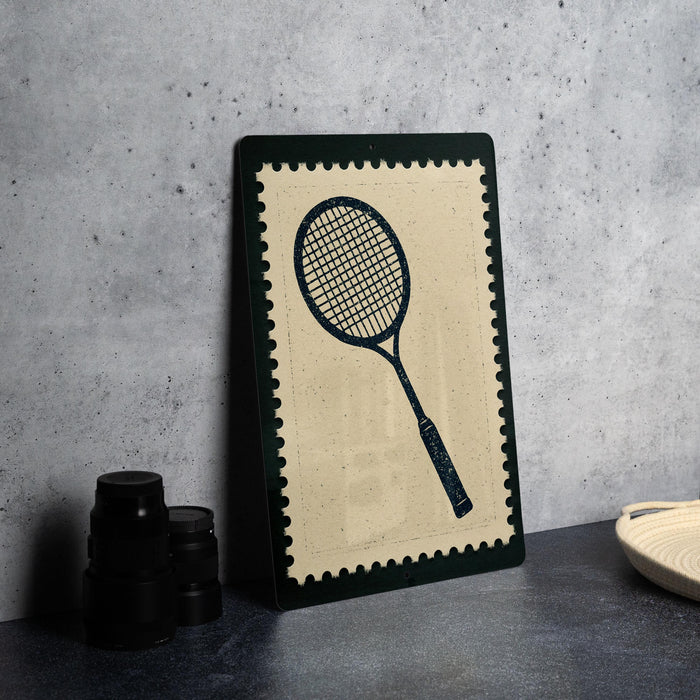 A framed tennis racket is displayed on a dark surface, with a stack of black camera lenses and a white dish visible to the right.
