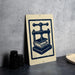 a sign with a blue and white design depicting a book press, placed on a gray countertop next to a stack of black camera lenses.