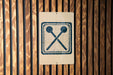a sign with a symbol of two crossed drumsticks on a wooden background.
