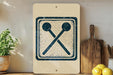 a kitchen counter with a wooden cutting board, a potted plant, and a sign with a symbol of two crossed spoons.