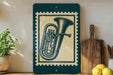 a framed illustration of a tuba on a shelf, with a potted plant to the left and a wooden cutting board to the right.
