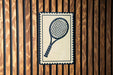 A tennis racket is displayed on a wooden wall, with a decorative border around it.