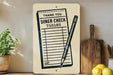 a sign with a list of items and a pencil, placed on a wooden surface next to a plant and some kitchen utensils.