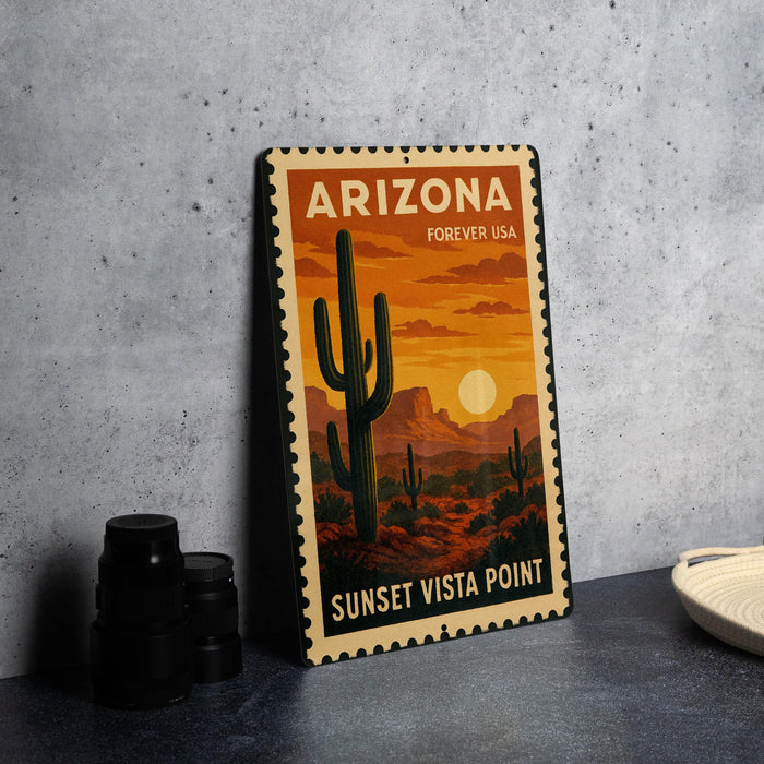 A vintage-style metal sign depicting a desert landscape with a cactus and a sunset, placed on a gray countertop next to some black camera lenses.