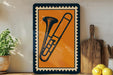 a framed illustration of a trombone on a wooden shelf, with a potted plant to the left and a wooden cutting board to the right.
