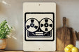 a white sign with a black and white graphic of a tape recorder, placed on a wooden surface next to a wooden cutting board and some lemons.