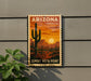 A vintage-style Arizona postage stamp featuring a desert landscape with a cactus and a sunset in the background, mounted on a wall.