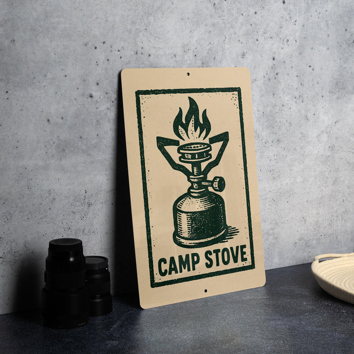 a sign with a green and black design depicting a camp stove, placed on a countertop next to some black camera lenses.