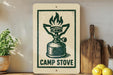 a sign with a green and white design depicting a camp stove, placed on a wooden surface next to a wooden cutting board and some lemons.