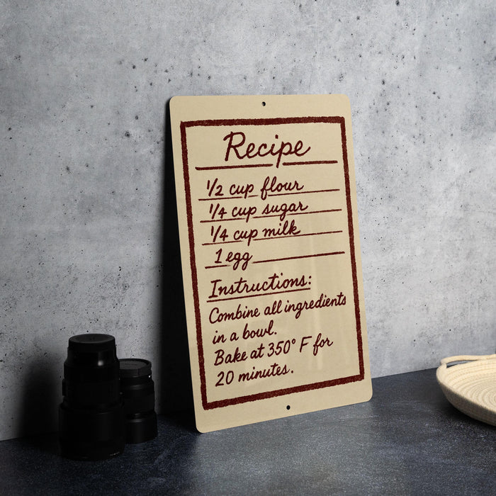 A recipe sign with handwritten instructions for baking a cake, placed on a kitchen counter next to some baking supplies.
