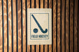 A sign indicating a field hockey area is mounted on a wooden wall.