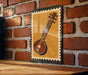 A framed image of a traditional Indian sitar, a stringed instrument, is displayed on a brick wall.