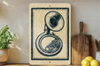 a vintage-style brass instrument, specifically a tuba, displayed on a shelf with a potted plant and a wooden cutting board nearby.