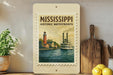 A framed poster of a Mississippi River with a lighthouse and a steamboat, displayed on a shelf next to a wooden cutting board and some lemons.
