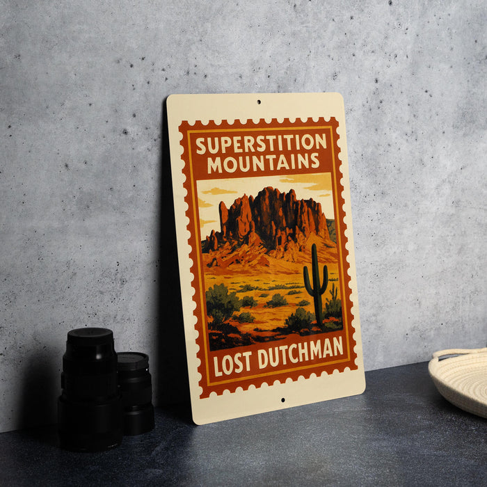 A vintage-style metal sign with a desert mountain landscape and a cactus, featuring the text "SUPERSTITIATION MOUNTAINS LOST DUTCHMAN".
