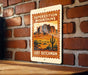 A vintage-style metal sign with a desert landscape and a cactus, mounted on a brick wall.