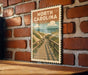 A vintage-style metal sign with the text "NORTH CAROLINA" is displayed on a brick wall, featuring a wooden boardwalk leading to a beach.