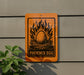an orange sign with a black and white illustration of a Phoenix egg, surrounded by flames, mounted on a gray wall.