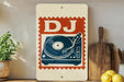 a vintage-style sign with a DJ turntable design, placed on a wooden surface next to a potted plant and a wooden cutting board.