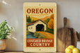 a vintage-style sign for the "Covered Bridge Country" in Oregon, with a wooden bridge and a scenic landscape in the background.
