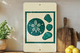 a framed artwork depicting a seashell with a flower design, placed on a shelf next to a wooden cutting board and a potted plant.