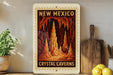 A framed poster of the Crystal Caves in New Mexico, featuring an illustration of the cave system with tall, orange rock formations.