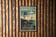 A Minnesota-themed poster featuring a lighthouse and the text "Lakeshare Lighthouses" is displayed on a wooden wall.