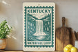 A sign for Kentucky's Waterfall Loop hangs on a wall, surrounded by kitchen utensils and a potted plant.