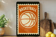 A vintage-style basketball sign with a bold orange and white design is displayed on a shelf, accompanied by a potted plant, a wooden cutting board, and some lemons.