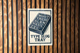 a sign with the text "Type Slug Tray" on it, mounted on a wooden wall.