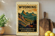A vintage-style stamp depicting a mountainous landscape with the text "Wyoming High Country Overlooks" is displayed on a wall, accompanied by a wooden cutting board and a potted plant.