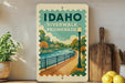A vintage-style sign for Idaho Riverwalk promenade, featuring a scenic illustration of a river, park, and walking path.