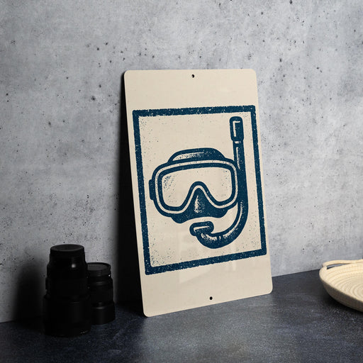 a sign with a blue and white illustration of a snorkel and mask, placed on a gray countertop next to some black camera lenses.