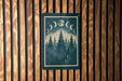 A framed poster depicting a night scene with a forest and crescent moon is hanging on a wooden wall.