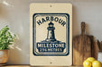 a sign with a lighthouse and the text "Harbour", along with the text "MILESTONE 256 METRES" indicating the distance to the lighthouse. The sign is displayed on a shelf, with a potted plant and a cutting board nearby.