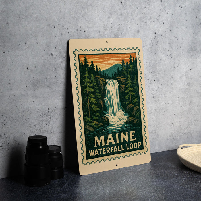 A framed illustration of a waterfall surrounded by pine trees, with the text "MAINE WATERFALL LOOP" on the frame.