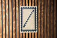 a sign with a stylized drawing of a pen or pencil on a white background, mounted on a wooden wall.