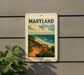 A framed poster of a beach scene with a bench and ocean in the background, mounted on a wall.