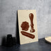 a beige sign with a brown illustration of a seal, a wax seal, and a wax stamp on it, placed on a gray countertop next to some black camera lenses.