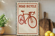 a vintage-style sign with a red bicycle illustration, placed on a wooden surface next to a potted plant and a wooden cutting board.