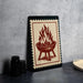 a framed illustration of a grill with flames on it, placed on a table next to some black containers.