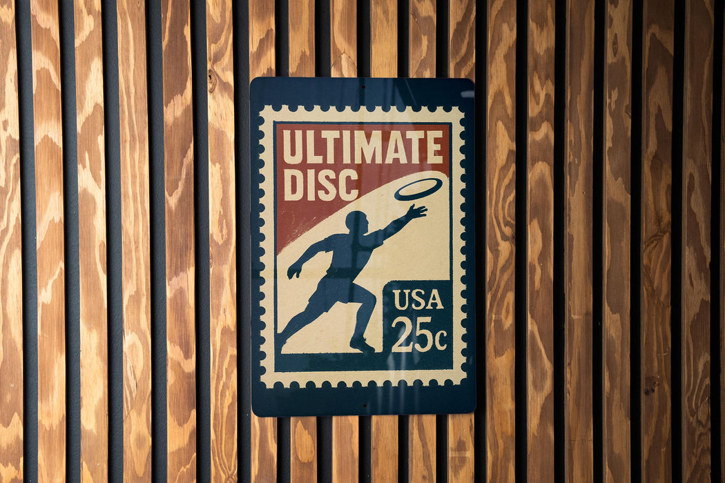 A sign that reads "Ultimate Disc" with a 25c postage stamp, mounted on a wooden wall.