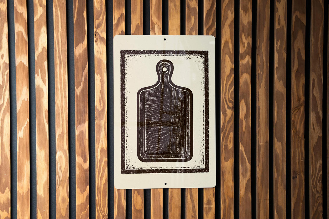 A sign with a black and white image of a cutting board is mounted on a wooden wall.