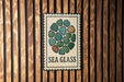 a sign with a circular design of green and brown stones, mounted on a wooden wall.
