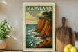 A framed postage stamp depicting a scenic coastal landscape in Maryland, with a cliff overlooking the ocean.