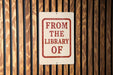 A sign that reads "FROM THE LIBRARY OF" is displayed on a wooden wall.