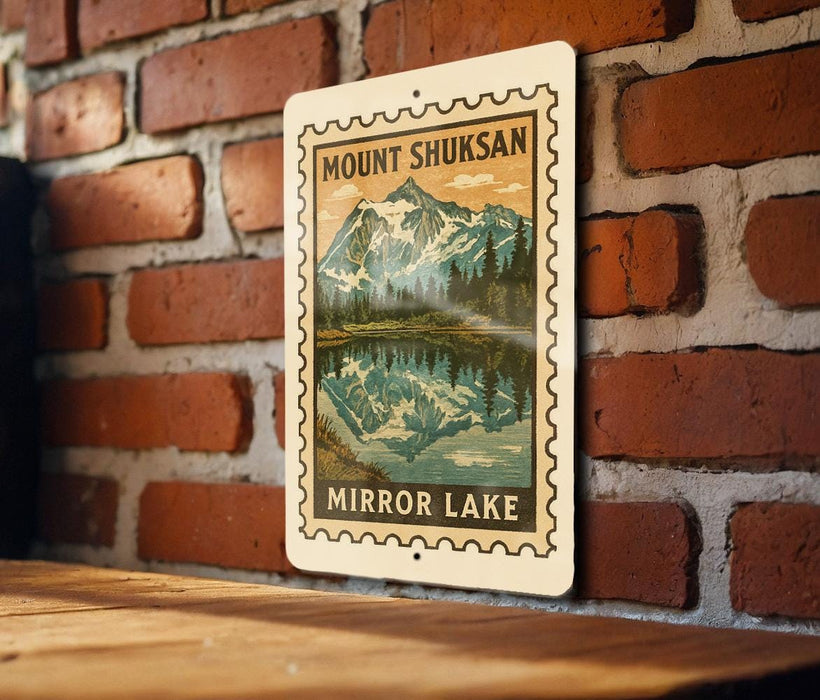 A metal sign with a mountain landscape and a lake, mounted on a brick wall.