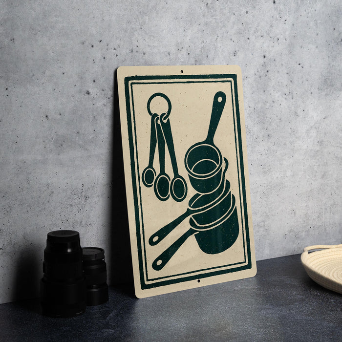a kitchen-themed sign with a black and green design, including a cup, a bowl, and a spoon, placed on a countertop next to some black containers.