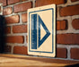 a sign with a blue triangle and a ruler on a brick wall.