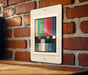 a colorful television antennae-like design displayed on a white frame, mounted on a brick wall.